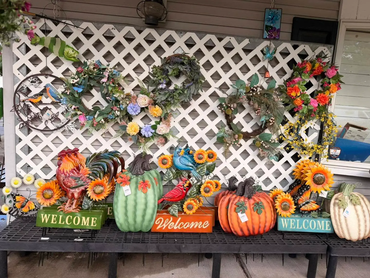Fall display of floral wreaths, metal pumpkins, roosters and Welcome signs on a bench